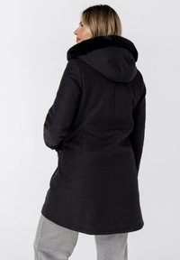 Donkergrijze jas met capuchon en nepbontafwerking. Heeft een getailleerd ontwerp, zijzakken en een gestructureerde stof.