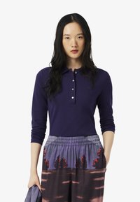 Polo shirt met lange mouwen in diep paars katoen, voorzien van een knoopsluiting en een klein logo, gecombineerd met kleurrijke, gemusterde broek.