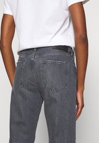 Jeans in denim grigio scuro con vestibilità rilassata, dotati di due tasche posteriori e di un'etichetta in pelle nera sulla vita.