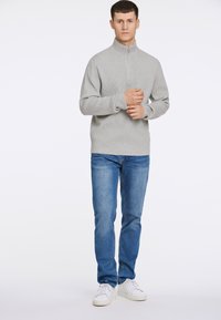 Ljusgrå,ribbade tröja med hög krage, med en framzipper. Kombineras med blå denimjeans och vita sneakers.