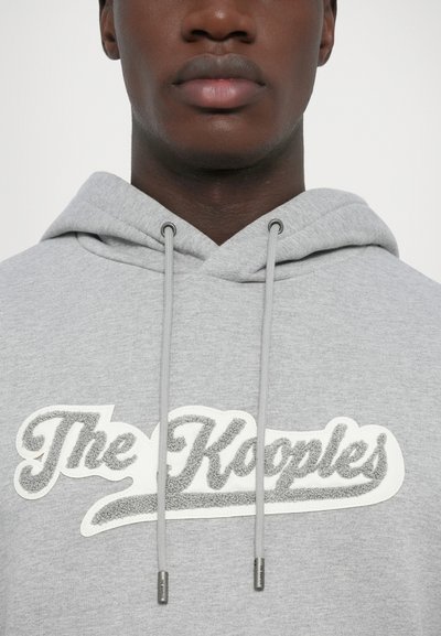 Hoodie gris en tissu doux, avec un cordon de serrage réglable et un logo texturé bien visible en blanc et gris sur la poitrine.