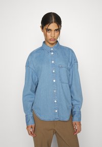 Camicia in denim azzurro chiaro con colletto, taschino anteriore e bottoni argentati. Presenta una vestibilità rilassata e maniche lunghe con polsini.