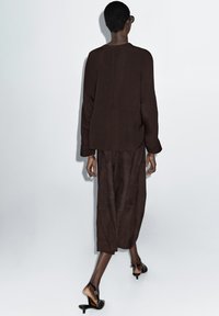 Brun lagdelt top med lange ærmer, parret med en matchende gulvlang nederdel. Glat stof og et minimalistisk design, båret med sorte hæle sandaler.