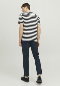 Gestreiftes T-Shirt mit navy-blauen und weißen horizontalen Streifen, kombiniert mit navy-blauen Slim-Fit-Hosen. Das Modell trägt dunkle Schuhe und wird von hinten betrachtet.