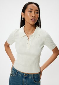 Licht beige geribde polo met korte mouwen, drie-knoopsluiting, aansluitend ontwerp, gecombineerd met high-waisted spijkerbroeken.