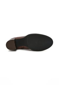 Suola di scarpa in pelle marrone con punta arrotondata e tacco basso. Suola in gomma nera testurizzata per una migliore aderenza, caratterizzata da un motivo a righe.