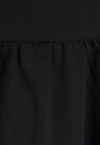 Černá tkanina s jemnou texturou, která na spodním okraji obsahuje nařasené detaily, čímž vytváří rozšířený siluetu.