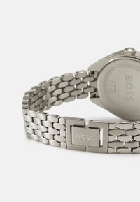 Montre en acier inoxydable argenté avec un bracelet à maillons et une boucle rectangulaire. Le dos affiche le logo de la marque "BOSS". Fini lisse.