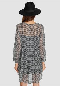 Vestido de espiga negro y blanco semitransparente con mangas largas, dobladillo en capas y escote redondo que presenta un cierre de botón en la parte posterior.