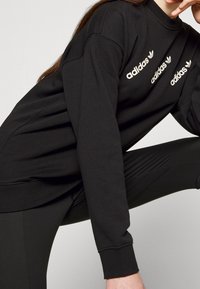 Black sweatshirt made of cotton-blend material, featuring a high neckline and three white Adidas logo accents on the front.