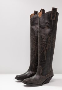 Botas altas de cuero negro con punta afilada, que presentan una superficie texturizada y un pespunte en zigzag en contraste a lo largo de la parte delantera, sobre un tacón de cuña.