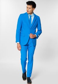 Heled sinine ülikond, millel on sobitatud bleiser ja vastahtavad püksid. Heleda sinise särgi ja lipsuga, mille kõrval mustad viisakad kingad.