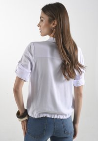 Witte blouse met korte opgerolde mouwen, voorzien van een gathered zoom. Soepele stof en minimalistisch ontwerp zonder versieringen.
