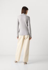 Svijetlosivi longsleeve s visokim izrezom, u kombinaciji s kremastim širokim hlačama i cipelama s uzorkom zmijske kože. Glatka tkanina, prilagođen dizajn.