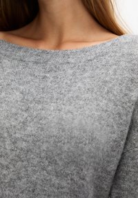 Pull en tricot gris avec un large décolleté décalé, texture douce et motif subtil, mettant en avant un design décontracté et relaxant.
