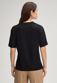 T-shirt noir à manches courtes avec une coupe décontractée, col rond et tissu lisse. La vue arrière montre un minimum de détails et une ligne d'ourlet droite.