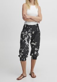 Czarne spodnie o kroju cropped z białym kwiatowym wzorem. Mają elastyczną talię i marszczone mankiety. Wykonane z lekkiego materiału.