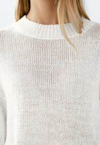 Witte gebreide trui met een ribbelkraag, een losse weefstructuur en subtiele horizontale patronen. Zacht en lichtgewicht materiaal.