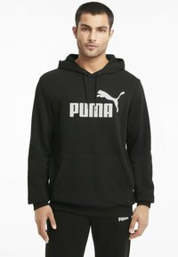 Hoodie noir en mélange de coton, avec un grand logo Puma blanc à l'avant et une poche kangourou. Manches longues avec des poignets côtelés.
