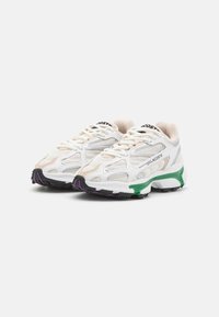Lacoste sneakers with a white mesh upper, green and purple accents, textured detailing, and a patterned black rubber outsole.