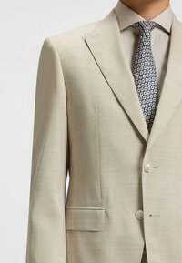 Beige skräddarsydd kavaj med texturerad yta, snittad krage, enknappsslutning och en passpojkficka på vänster sida.