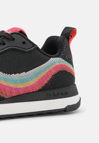 Baskets en mesh noir avec un motif ondulé multicolore en rose, bleu et jaune ; elles comportent une semelle en caoutchouc noire et des accents texturés.