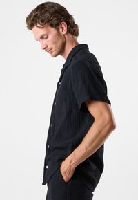 Sort kortærmet skjorte med knapper, lavet af tekstureret stof med en enkelt brystlomme, udstyret med knapper og designet med en afslappet pasform.