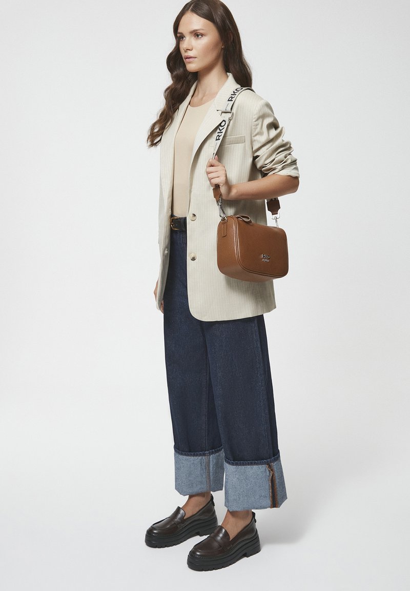 Beżowa marynarka w paski na beżowej bluzce, ciemnoniebieskie szerokie dżinsy z denimu z mankietami, oraz brązowa torba na ramię. Masywne brązowe mokasyny.