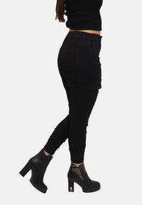 Zwarte cargobroek met een nauwsluitend ontwerp en zijzakken, gecombineerd met zwarte enkellaarsjes met hoge hak en een gestructureerd accent.