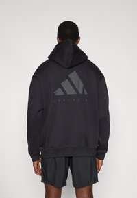 Μαύρο φούτερ με κουκούλα, με μεγάλο γκρι λογότυπο Adidas και τη λέξη "TRAINING" στην πλάτη. Διαθέτει χαλαρή εφαρμογή και ριμπ μανσέτες.