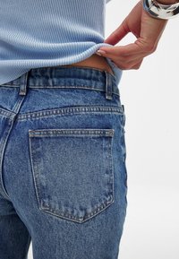 Blue denim jeans with a faded finish, featuring two back pockets and a mid-rise waist. The fabric has a smooth texture.