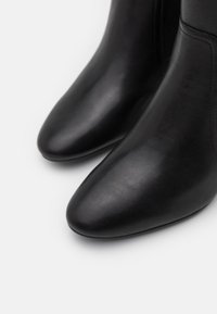 Bottines noires en cuir avec des pointes aiguës et une texture lisse. Elles présentent des coutures minimales et un design épuré sans embellissements.