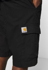 Shorts cargo noirs en tissu léger, dotés d'une poche latérale et d'un grand patch logo jaune Carhartt.