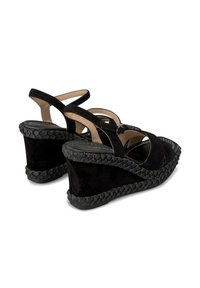Schwarze Wildleder-Wedge-Sandalen mit überkreuzten Riemen und geflochtenen Details entlang der Sohle. Glatte Innenauskleidung und strukturierter Absatz.