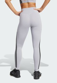 Leggings de tiro alto en gris claro, fabricadas con material elástico y con rayas laterales negras. Cuentan con una textura suave y un diseño ajustado, ideales para la ropa de actividad.