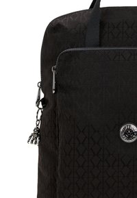 Borsa nera con un motivo a diamante testurizzato, chiusura con zip e un ciondolo decorativo nero. Include un accent metallic rotondo con logo.