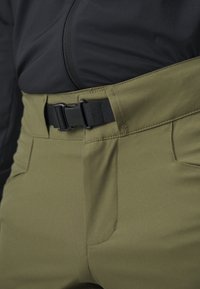 Olivgrüne Hose mit schlankem Design und schwarzem Schnallengürtel. Hergestellt aus einem glatten Stoff, mit flachen Fronttaschen und gesteppten Nähten.