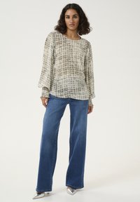 Haut léger et fluide de couleur claire avec un motif texturé en grille, associé à un jean bleu à jambes larges et des chaussures argentées à bout pointu. Manches longues évasées.