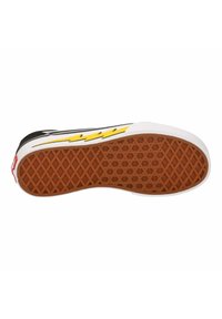 Sola di sneaker nera con un motivo a nido d'ape, con un bordo bianco e un design a saetta gialla; accento rosso vicino al tallone.