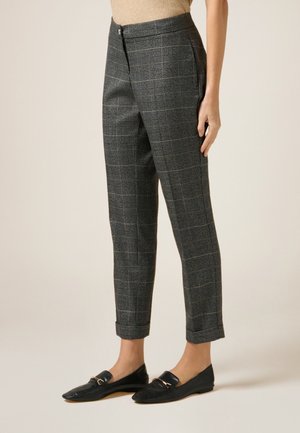 Pantalon gris à carreaux avec une coupe ajustée, présentant un devant plat, des poches latérales et une longueur cheville. Porté avec des mocassins noirs.