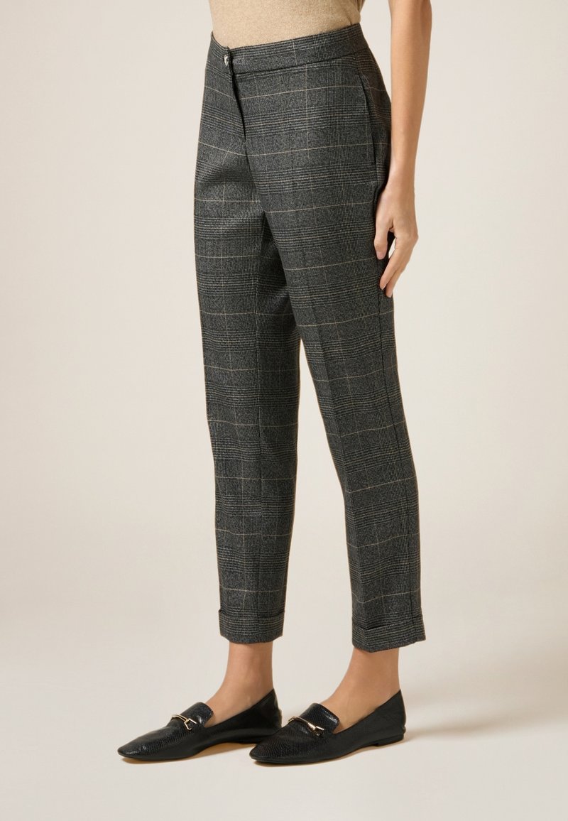 Pantalon gris à carreaux avec une coupe ajustée, présentant un devant plat, des poches latérales et une longueur cheville. Porté avec des mocassins noirs.