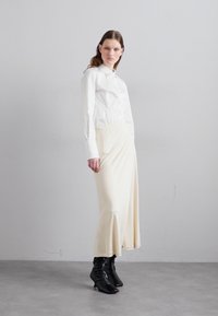 Camicia bianca con colletto, abbinata a una gonna midi fluida color crema e stivali neri alla caviglia. Tessuto morbido e silhouette aderente.