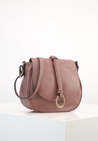 Różowa skórzana torebka crossbody o zaokrąglonym kształcie, z teksturowanym paskiem, złotymi detalami i magnesowym zapięciem, leżąca na białej powierzchni.