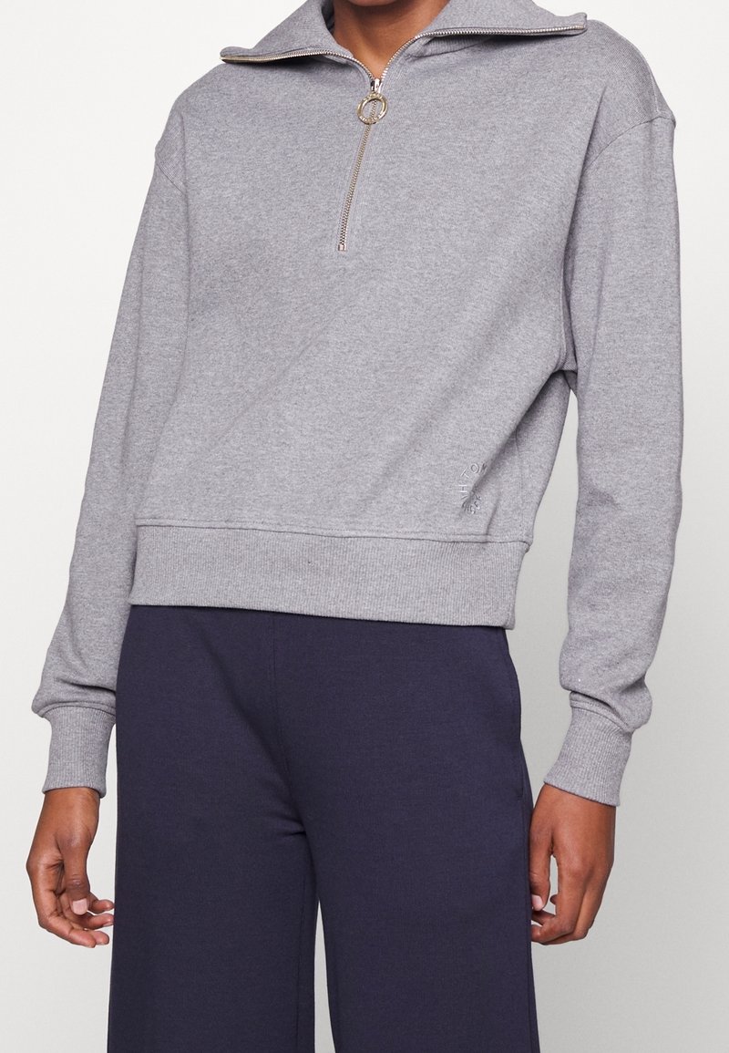 Pullover in pile grigio con collo a zip a un quarto e tirazip circolare. Presenta polsini e orlo a costine, con un discreto dettaglio del logo sul lato.