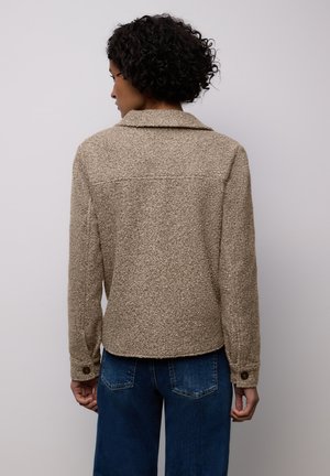 Chaqueta texturizada beige con cuello, mangas largas y puños abotonados. Combinada con denim azul, mostrando un ajuste relajado y vista trasera.