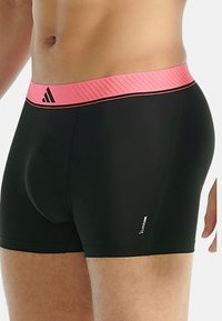 Svarta boxerkalsonger med en rosa ribbad midja, med en logo på den nedre sidan. Tyget ser slätt och åtsittande ut.