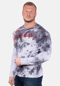Langärmliges Hemd in Grau mit schwarzem Tie-Dye-Muster, ausgestattet mit roten und goldenen grafischen Akzenten über der Brust und einem Rundhalsausschnitt.