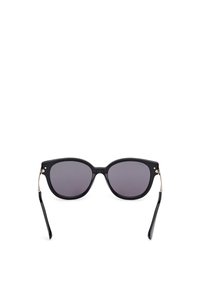 Gafas de sol negras con forma de ojo de gato, lentes oscuros y finos acentos de metal plateado en las patillas. Textura de plástico suave.