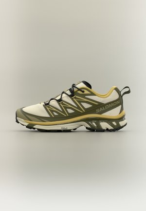 Sportschuh mit atmungsaktivem weißem Mesh-Obermaterial, olivgrünen Akzenten, strukturiertem Außensohle und schwarzen Schnürsenkeln. Verfügt über eine gepolsterte Sohle und eine Zuglasche.