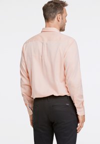 Camisa de manga larga rosa claro con un collar estructurado y puños abotonados, combinada con pantalones negros que cuentan con bolsillos traseros y un diseño elegante.